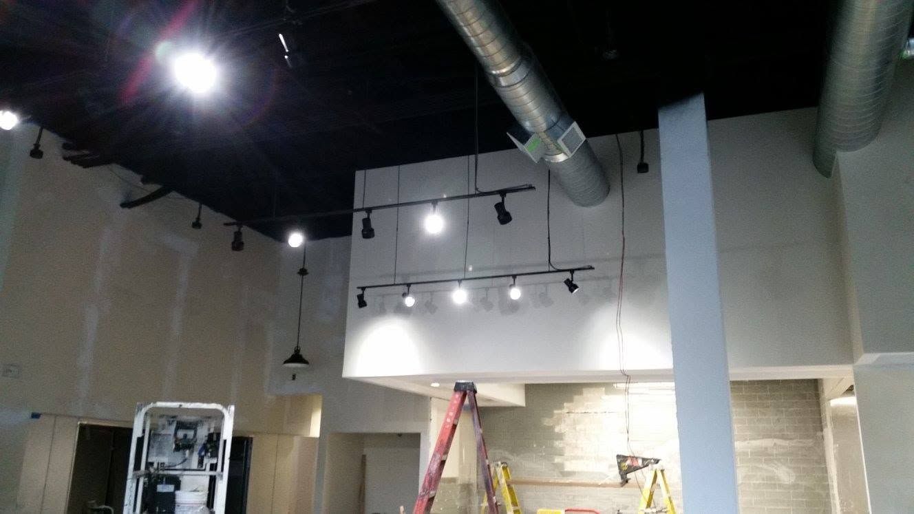 Industrial interior with black ceiling, ductwork, track lights, and ladders during construction