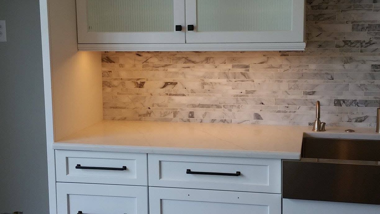 White kitchen cabinets with light wood countertop and stone backsplash, partially visible black sink on the right.