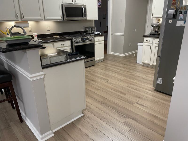 A kitchen with hardwood floors, white cabinets, a stove, microwave and refrigerator.