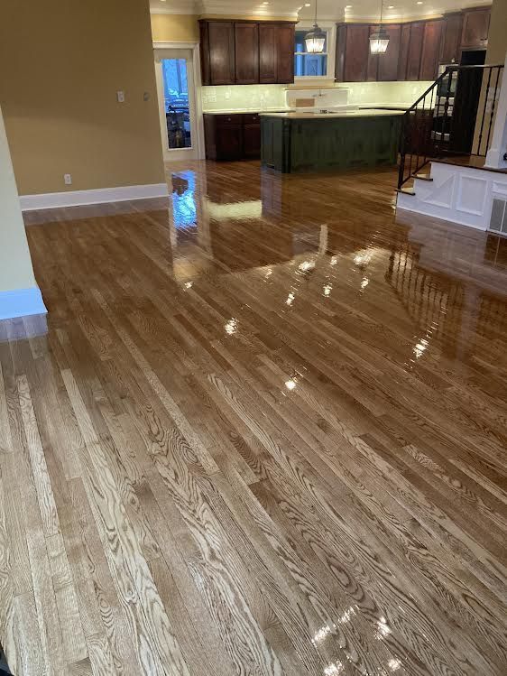 A living room with hardwood floors and a kitchen in the background.
