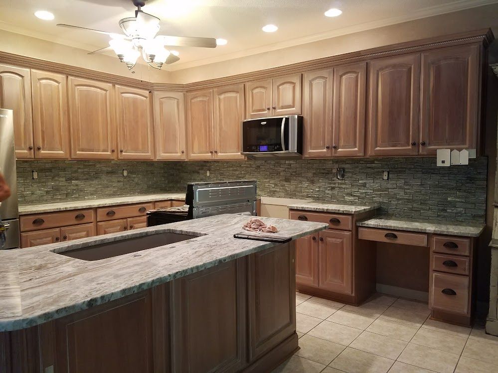 A kitchen with wooden cabinets , granite counter tops , a sink and a microwave.