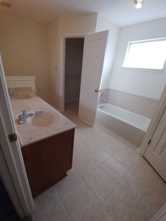 A bathroom with two sinks , a tub and a window.
