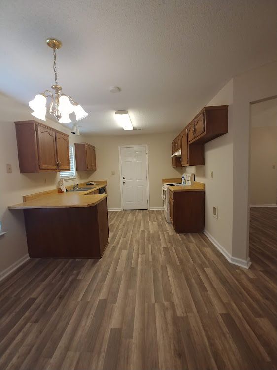 An empty kitchen with hardwood floors and wooden cabinets.