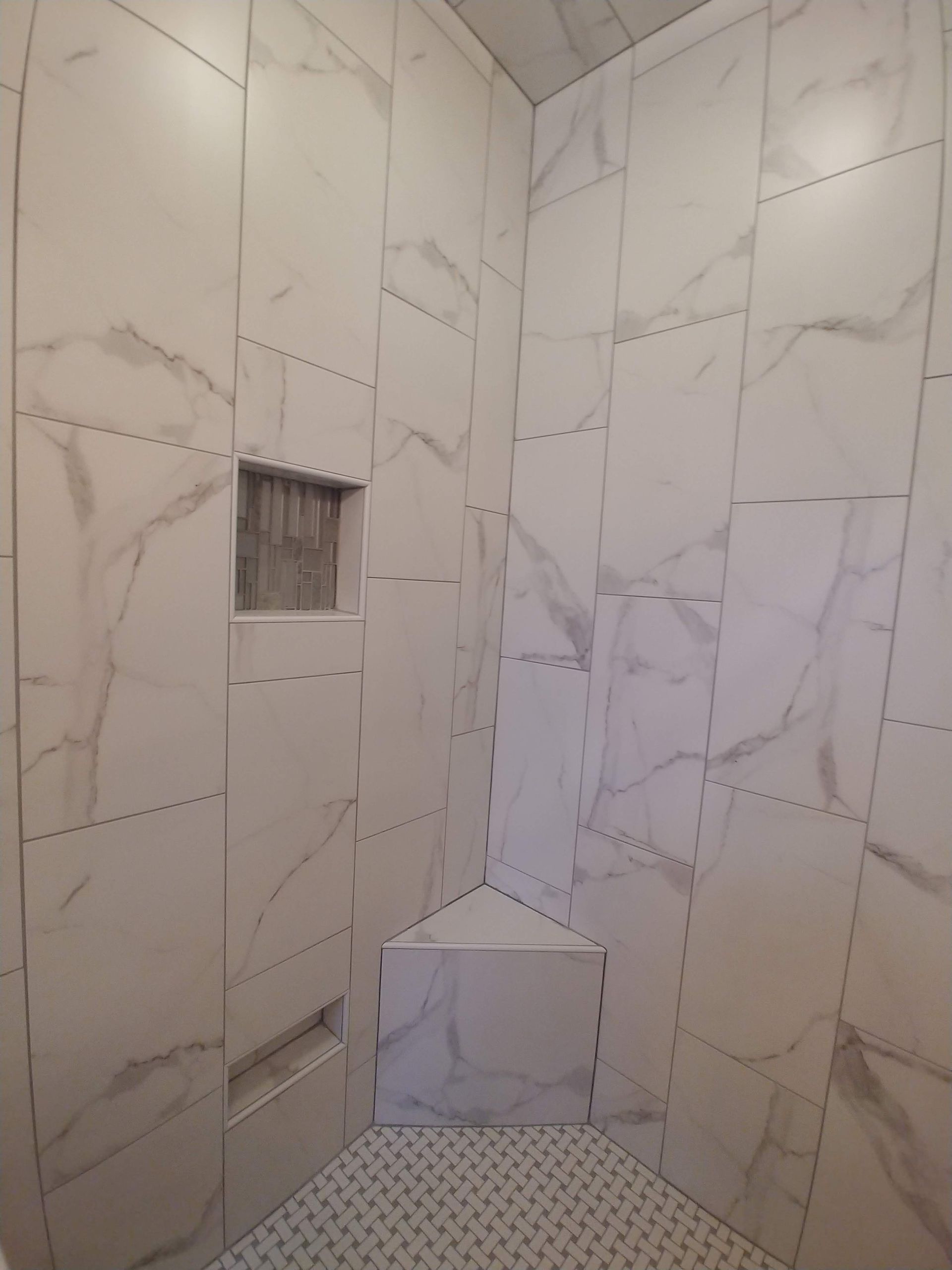 A bathroom with white tiles and a corner shower seat.