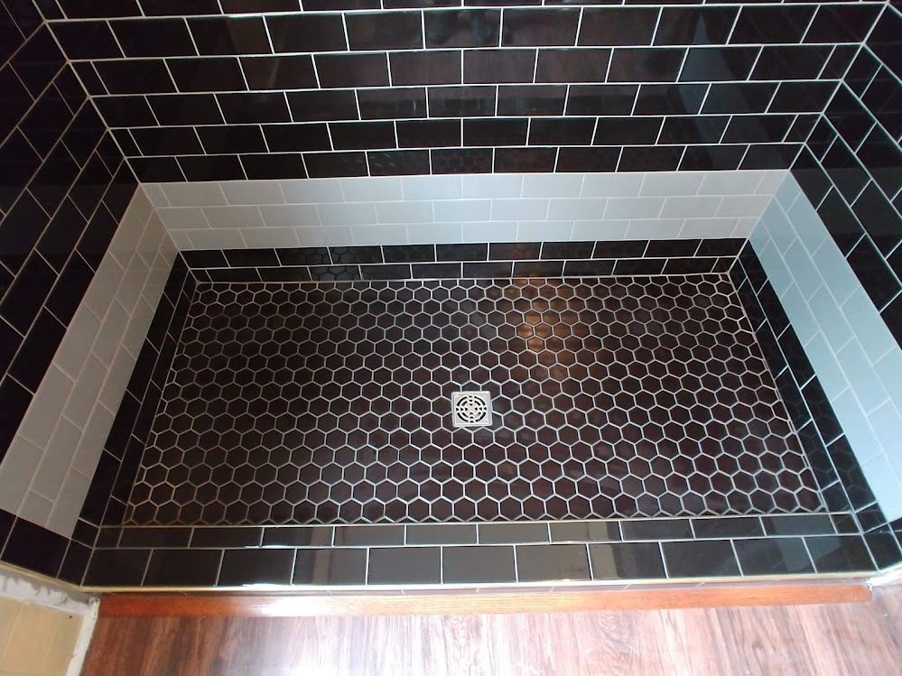 A shower stall with black and white tiles and a drain