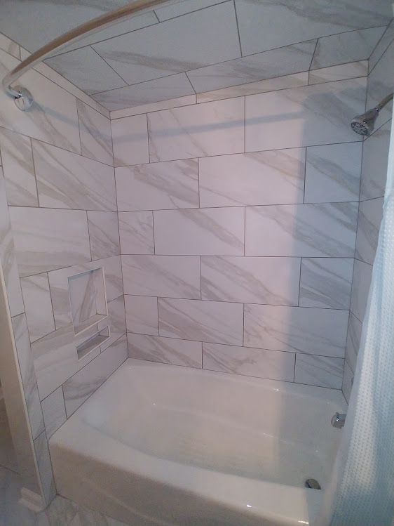 A bathroom with a bathtub , shower , and tiled walls.