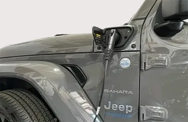 Gray Jeep Wrangler Sahara, charging port open, electric charger plugged in.