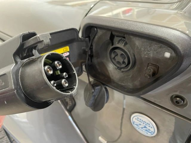 Close-up of an electric vehicle charging port with a connector ready to plug in. Gray car exterior.