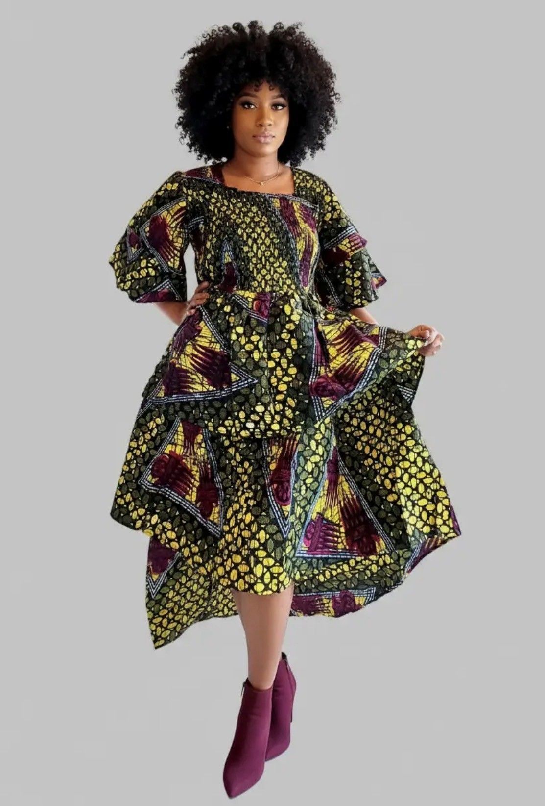 Woman in patterned dress with tiered skirt, holding dress hem. Burgundy booties.