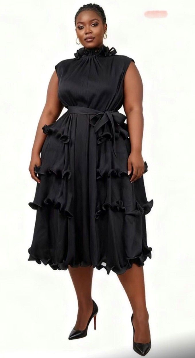 Woman in a black dress with ruffled skirt, high neck, and heels poses.