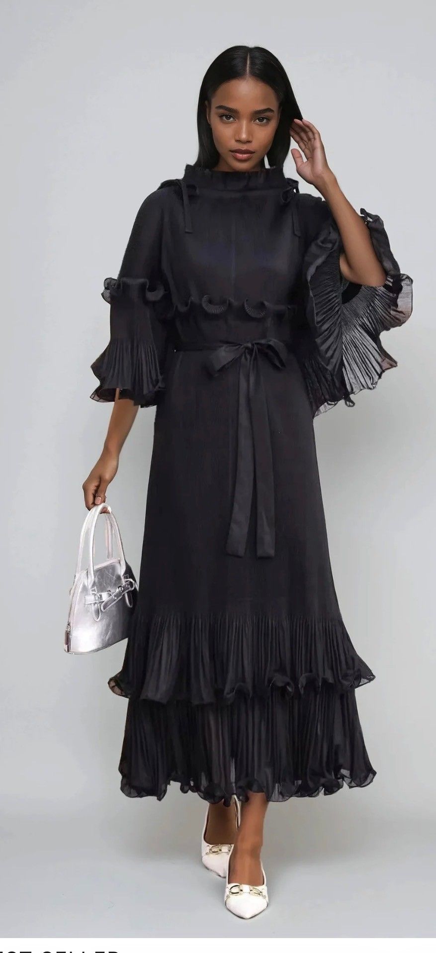 Woman in black dress with ruffled sleeves, high neckline, and tiered skirt, holding a silver bag.