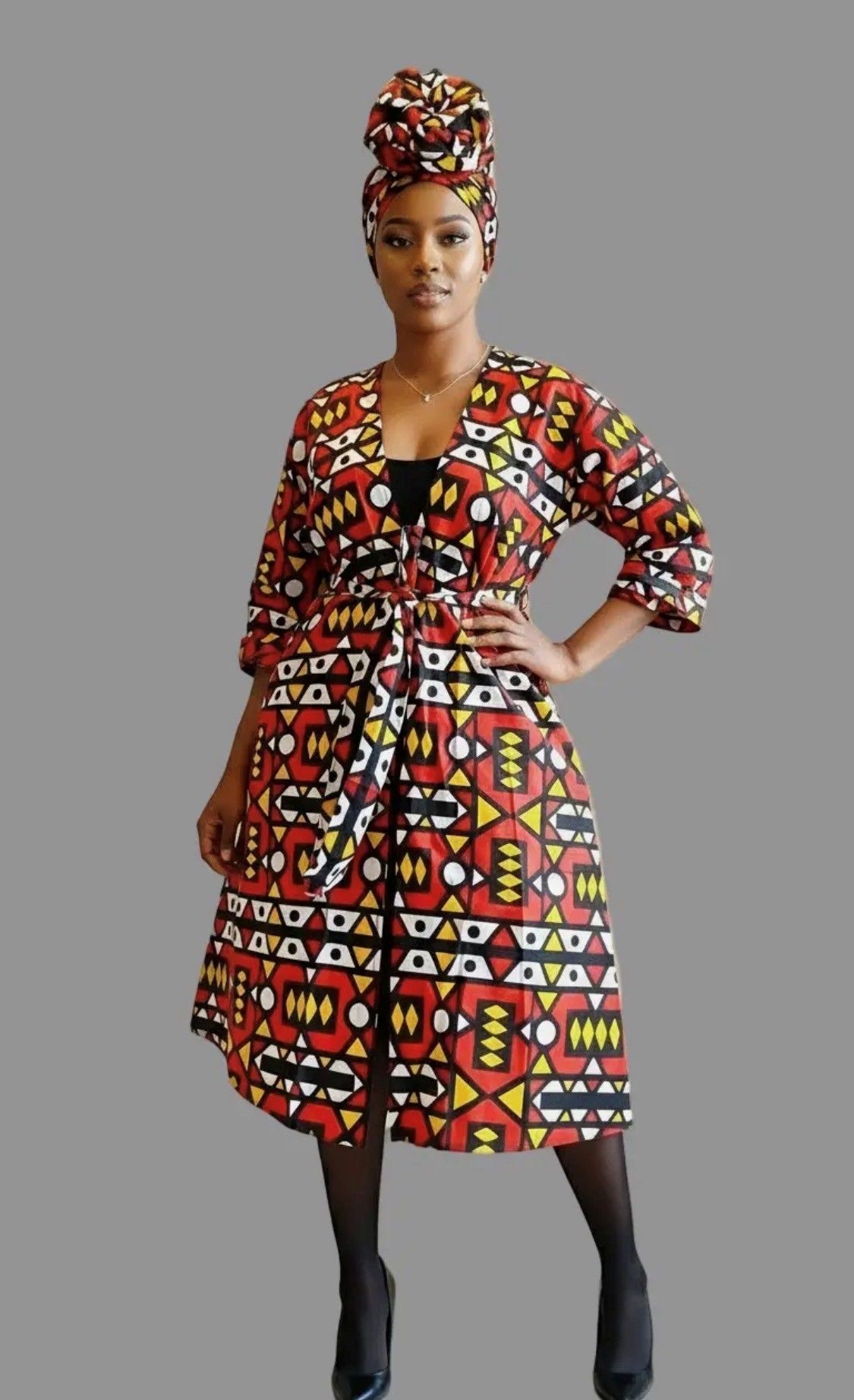 Woman wearing patterned African print jacket and headwrap, posing with a hand on hip.