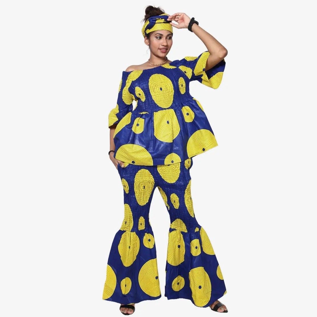 Woman in blue and yellow African print outfit, off-shoulder top, flared pants, and head wrap.