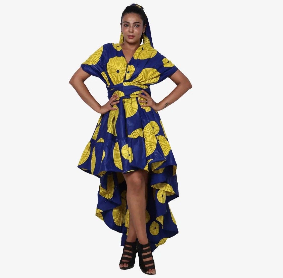 Woman in blue and yellow patterned dress with high-low hem and matching headscarf, hands on hips.
