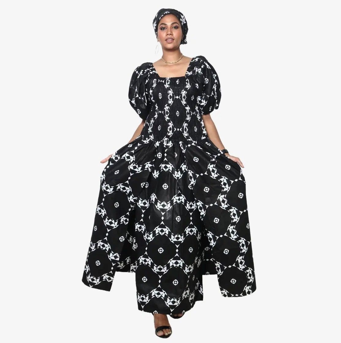 Woman in a black and white floral print maxi dress and head wrap, holding out the sides of the skirt.