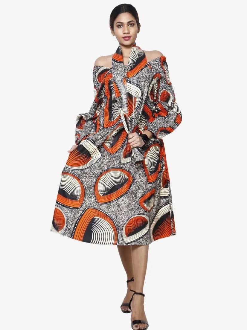 Woman in colorful off-shoulder patterned dress and heels, posing in front of a white background.