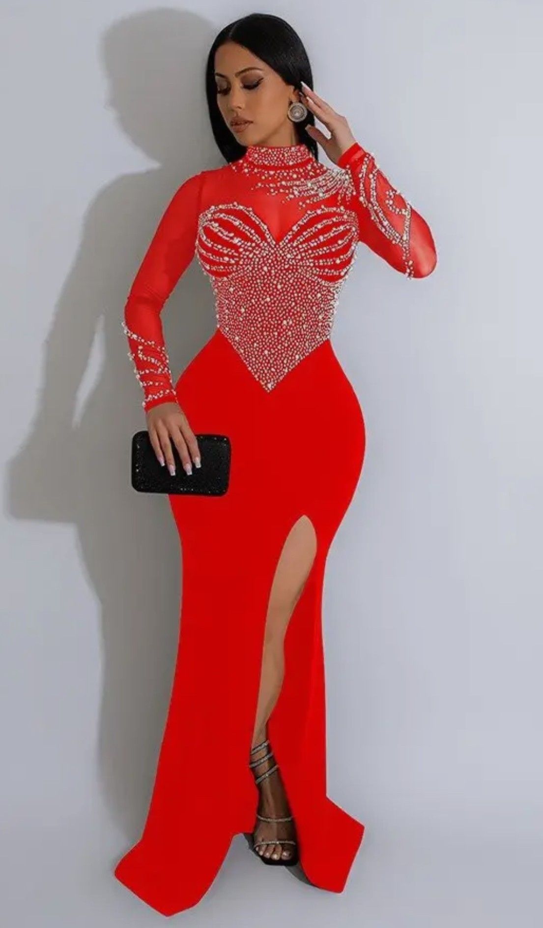 A woman is wearing a red dress with a high slit and holding a black clutch