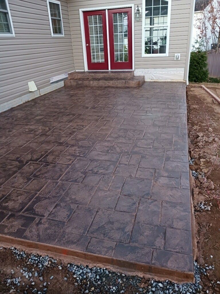 Brown stamped concrete patio with steps leading to red double doors of a house.