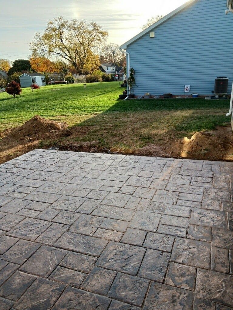 Stamped concrete patio next to a house with a grassy lawn, under a sunny sky.