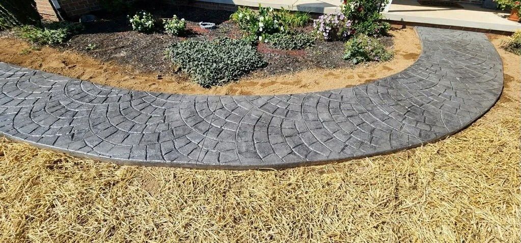 Curved stone pathway through a grassy yard, leading towards a flower bed.