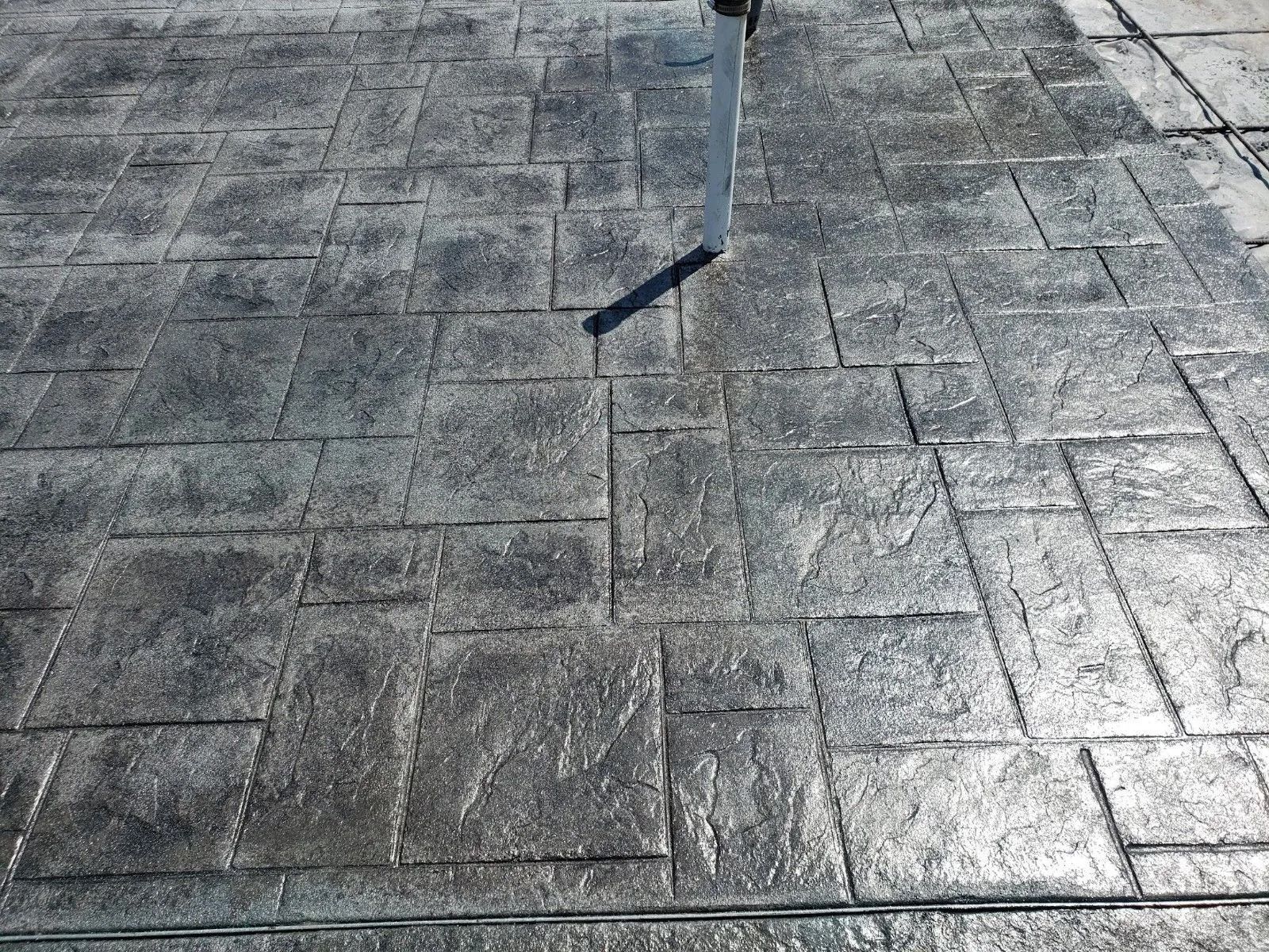 Stamped concrete patio in a brick pattern, gray with shiny sealant.