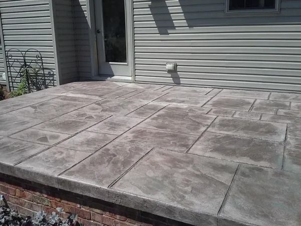 Gray stamped concrete patio with brick base, next to a light-colored building with a door.