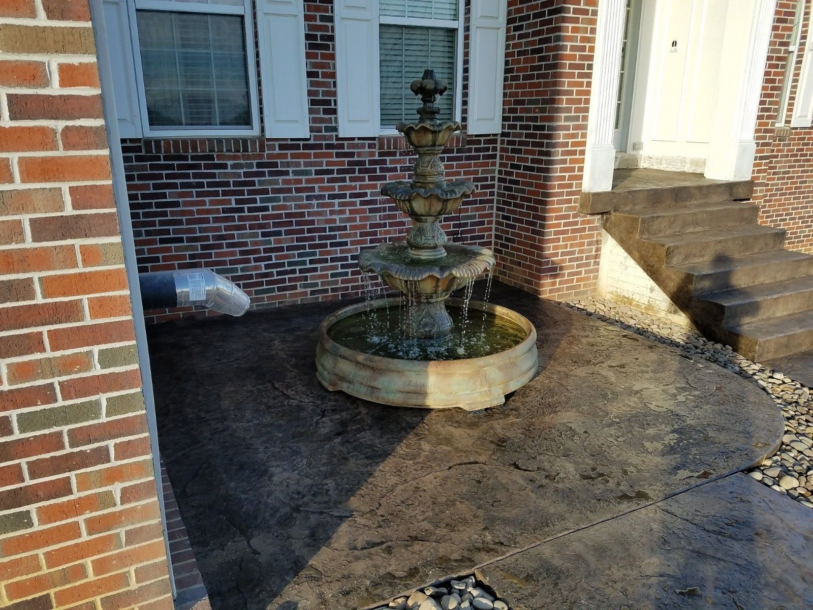 A tiered fountain on a concrete patio in front of a brick house.