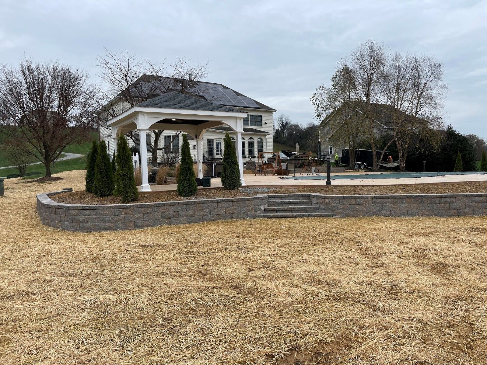 Outdoor pavilion with raised seating area, house in background, cloudy sky.
