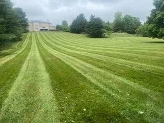 Green lawn with striped mowing pattern leading up to a large house on a cloudy day.