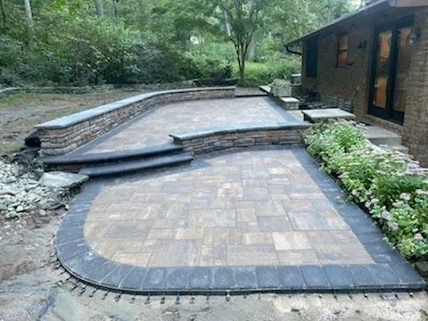 Paver patio with stone retaining walls, steps, and house in background.