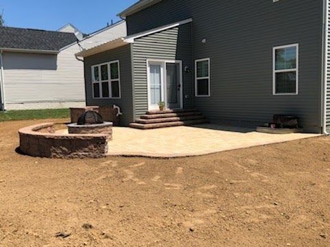 Backyard patio with fire pit, steps, and house with gray siding. Brown dirt surrounding.