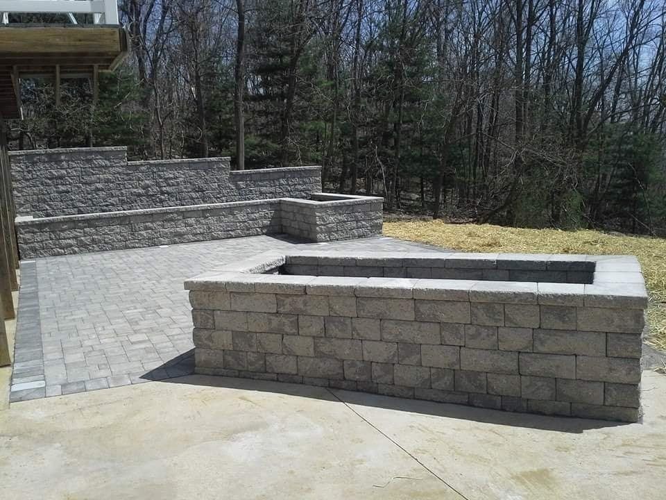 Stone patio with retaining walls and built-in planters, leading to a wooded area.