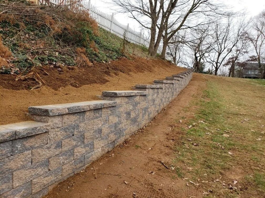 Stone retaining wall on a hillside with brown soil and sparse vegetation.