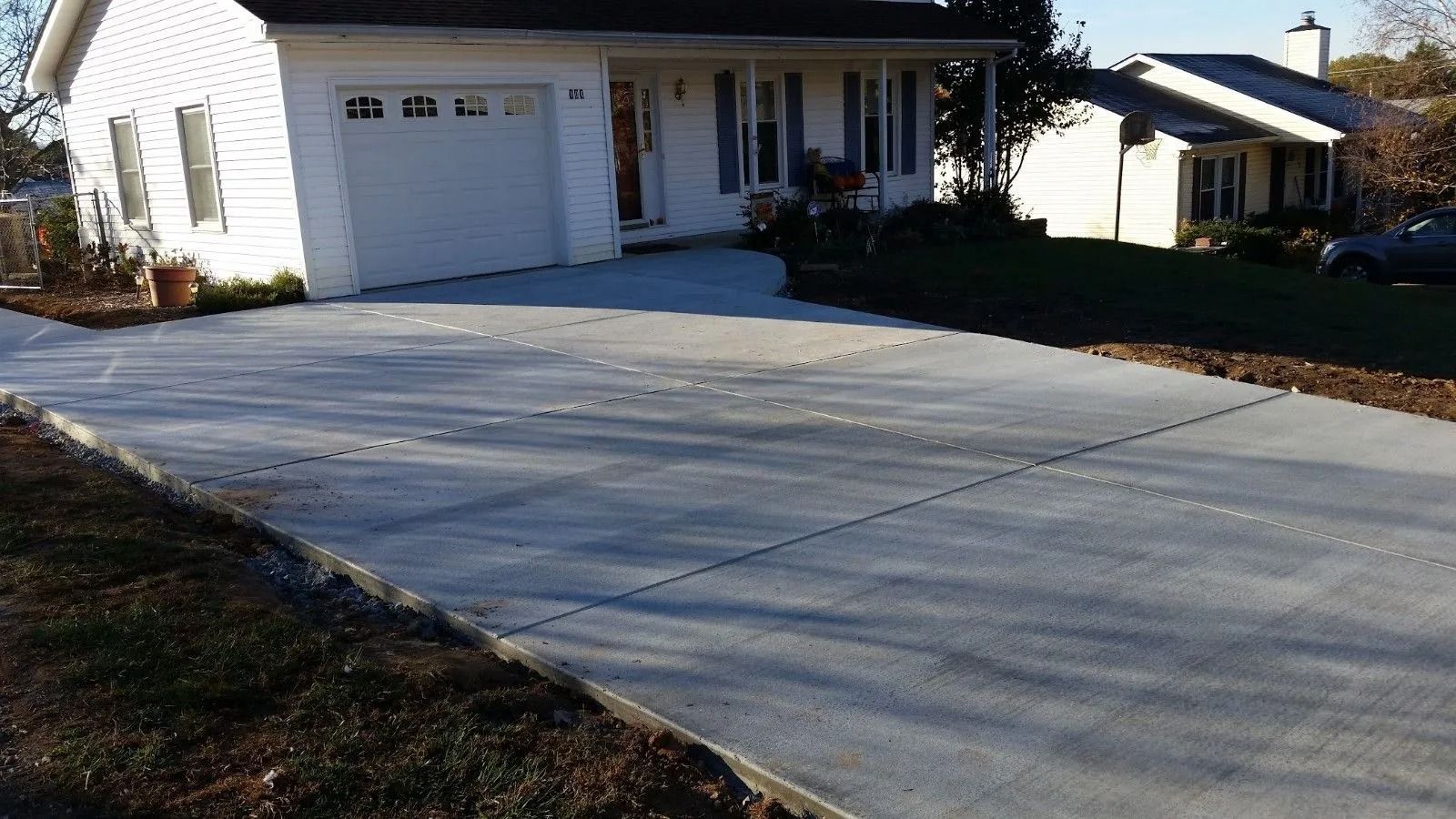 Newly poured concrete driveway in front of a white house with a garage and a front porch.