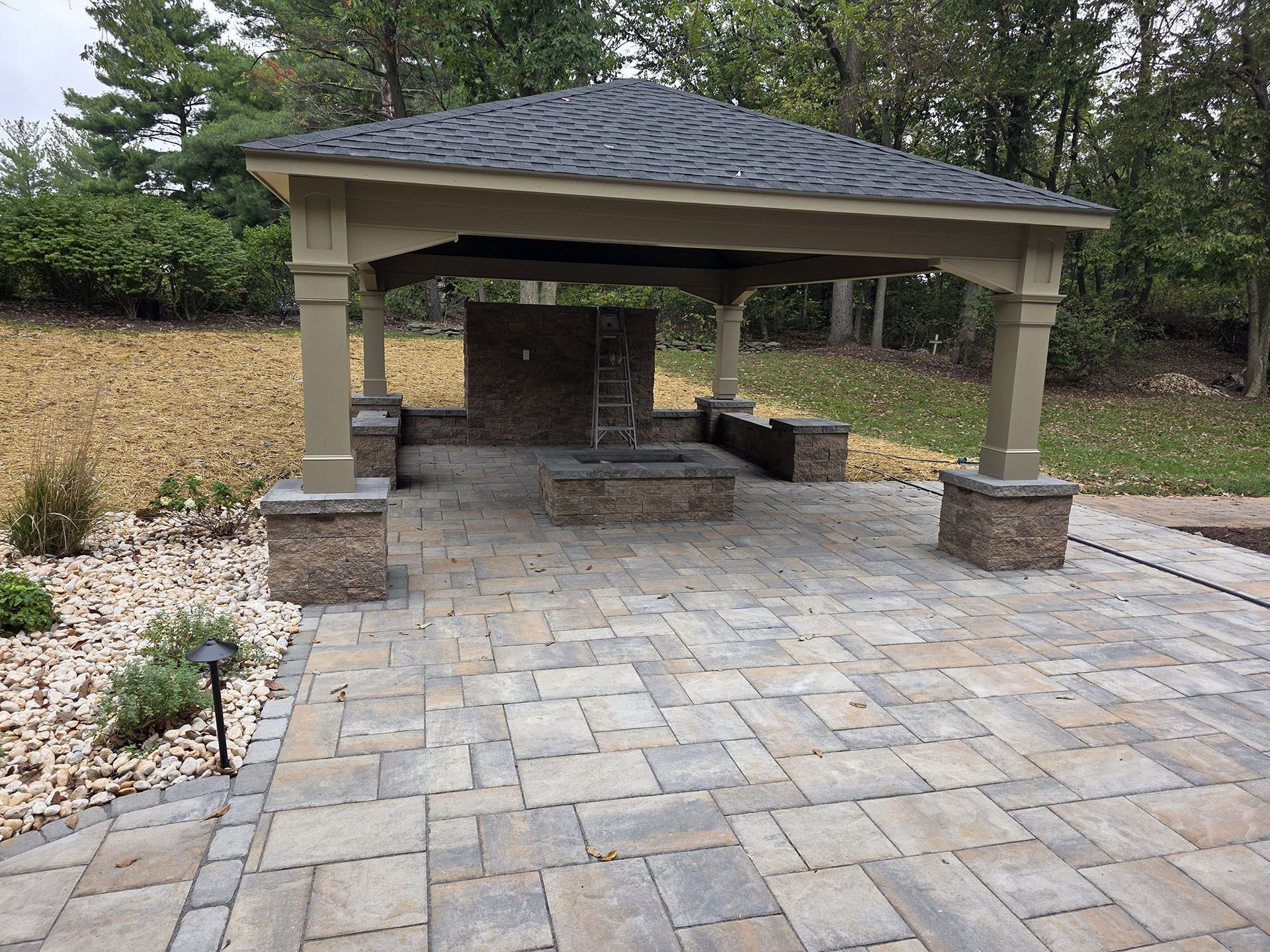 Patio with a pavilion, fire pit, and stone pavers in a backyard setting.