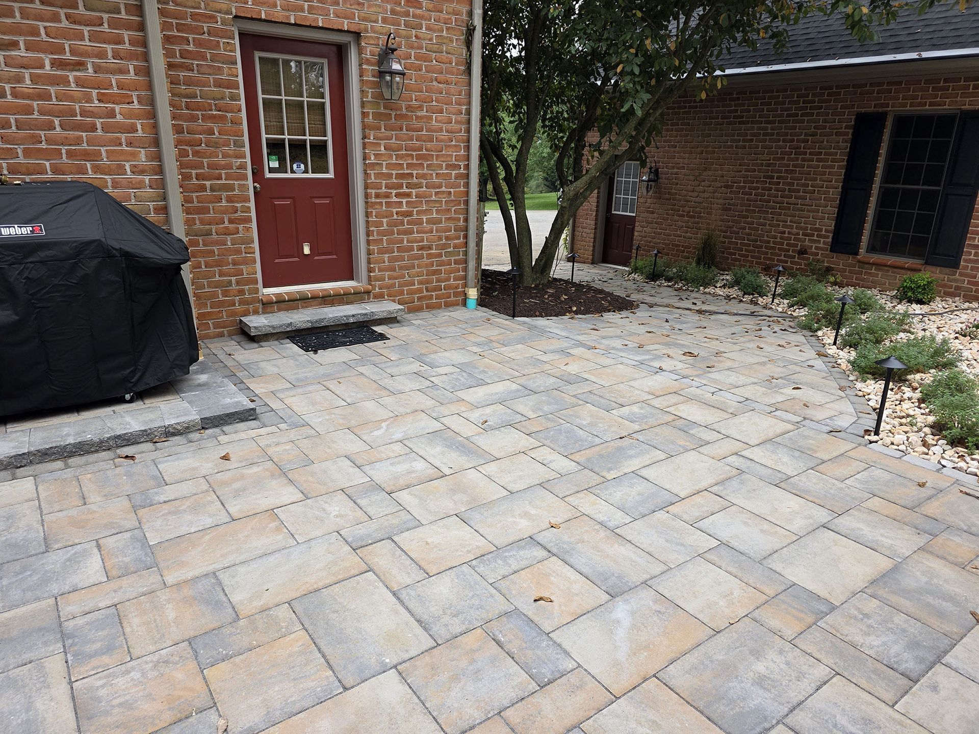 Brick patio with a red door and a grill covered with a black cover.