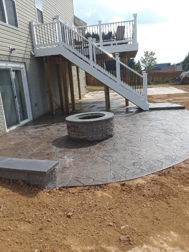 Stamped concrete patio with a fire pit and stairs leading to a deck on a house.