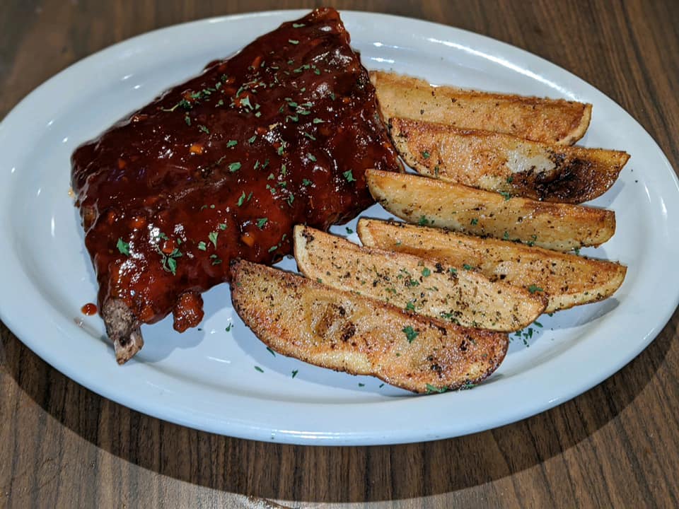A white plate topped with ribs and potato wedges