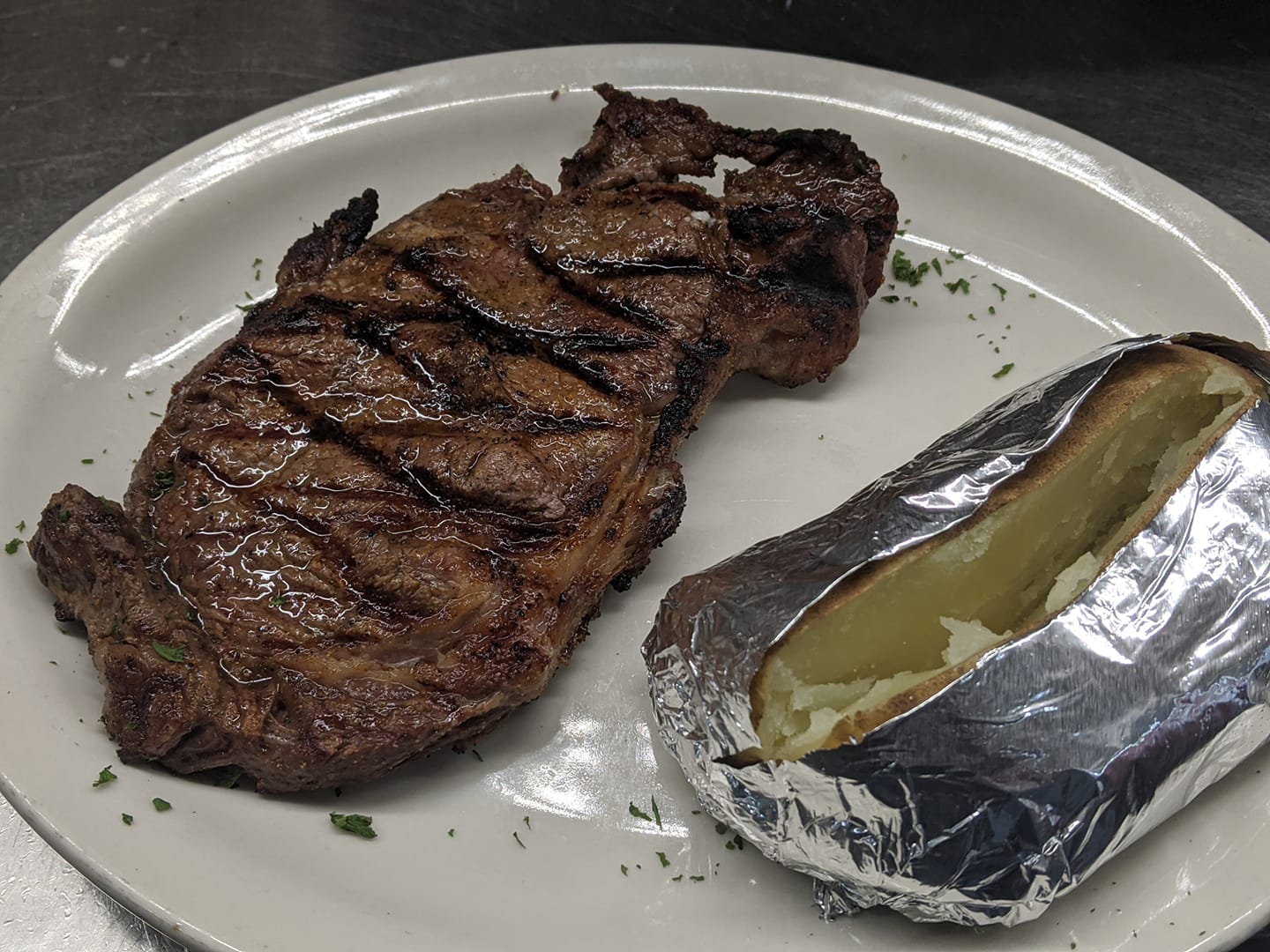 A white plate topped with a steak and a baked potato
