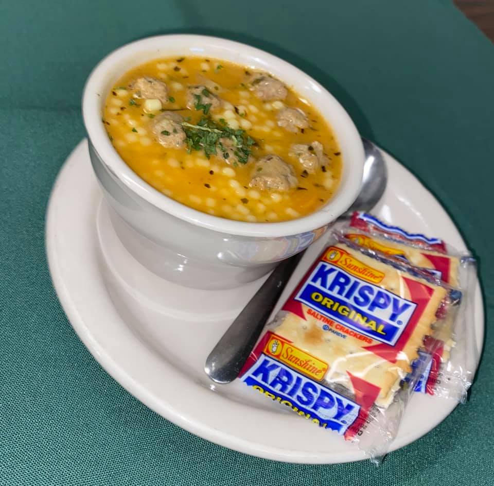 A bowl of soup next to a bag of krispy crackers