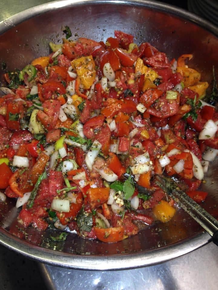 A metal bowl filled with tomatoes , peppers , onions and other vegetables.