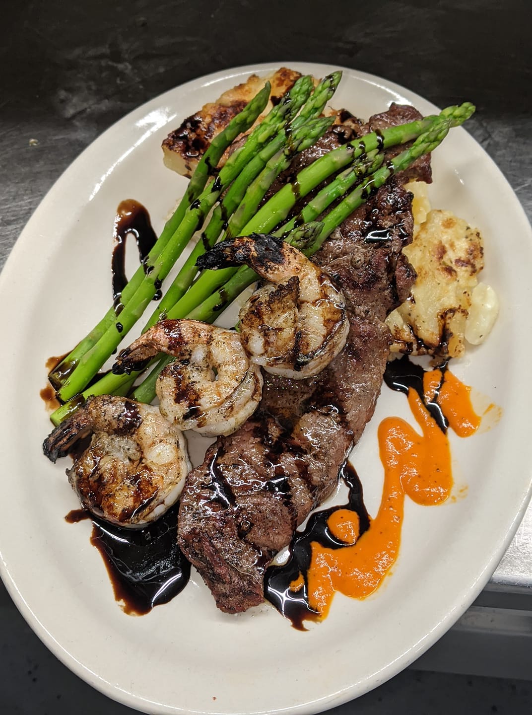 A white plate topped with meat , shrimp , asparagus and potatoes.