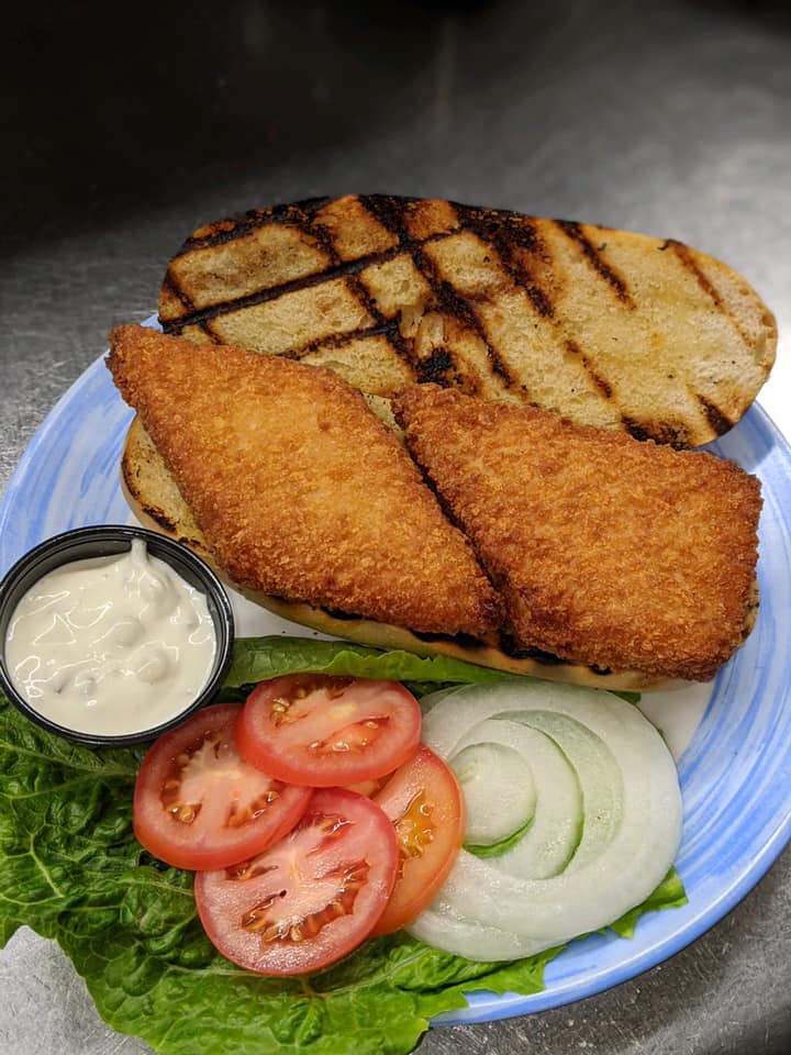 A fish sandwich with lettuce , tomatoes , onions and mayonnaise on a blue plate.