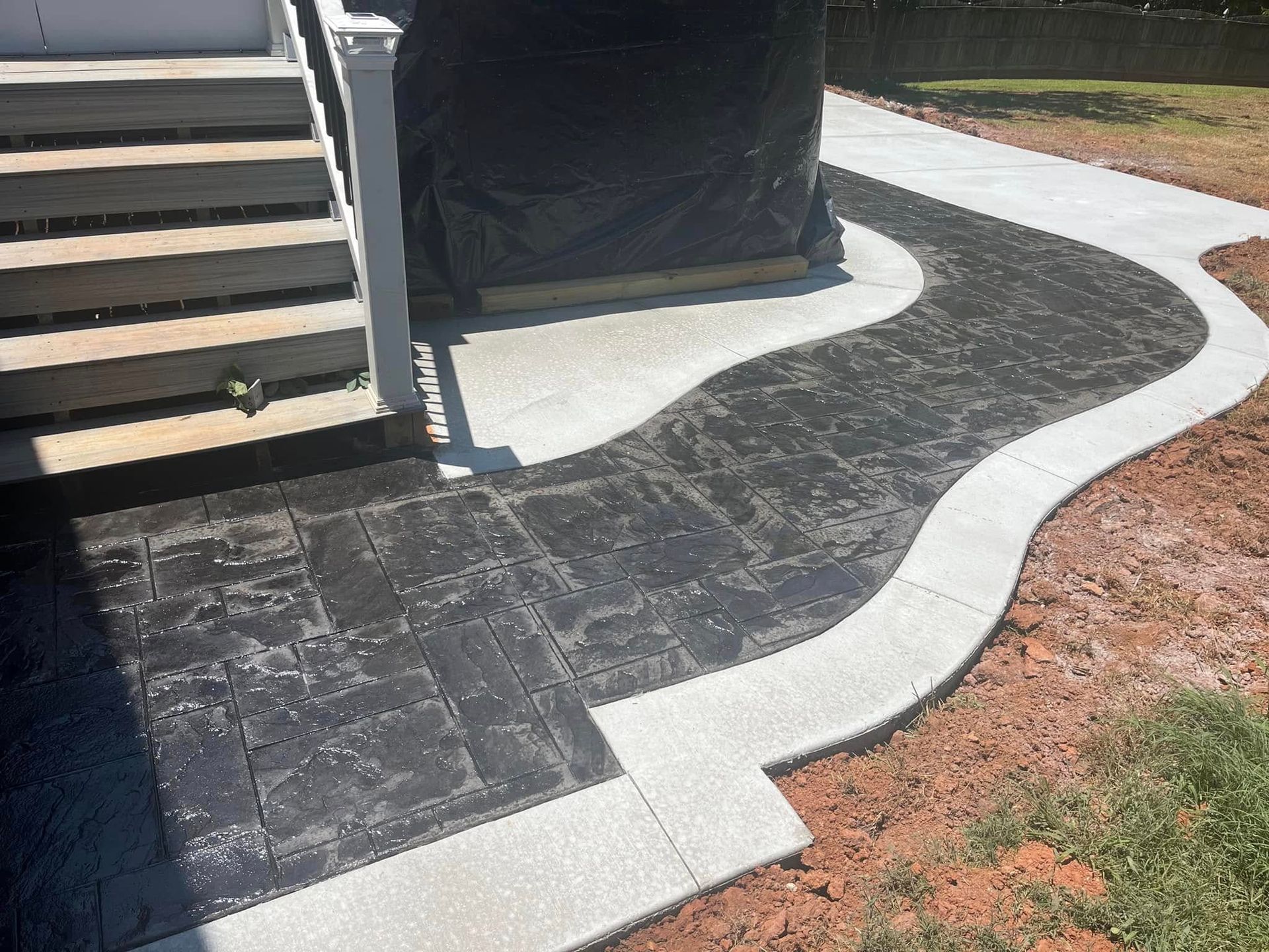 A curved stamped concrete walkway with a dark textured path bordered by light gray concrete steps and edges.