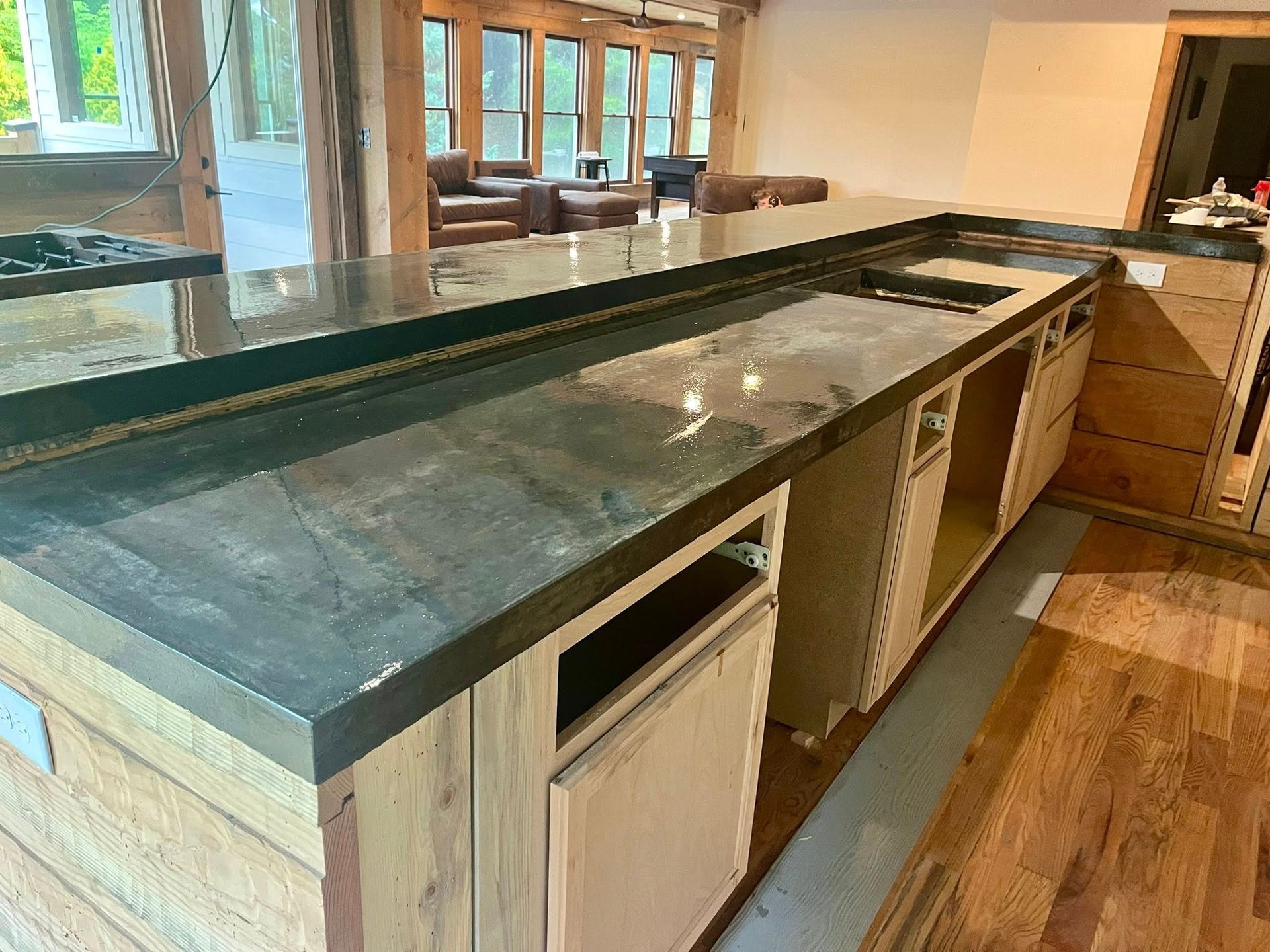 A kitchen island under construction with dark soapstone countertops, unfinished wooden cabinets, and hardwood floors.