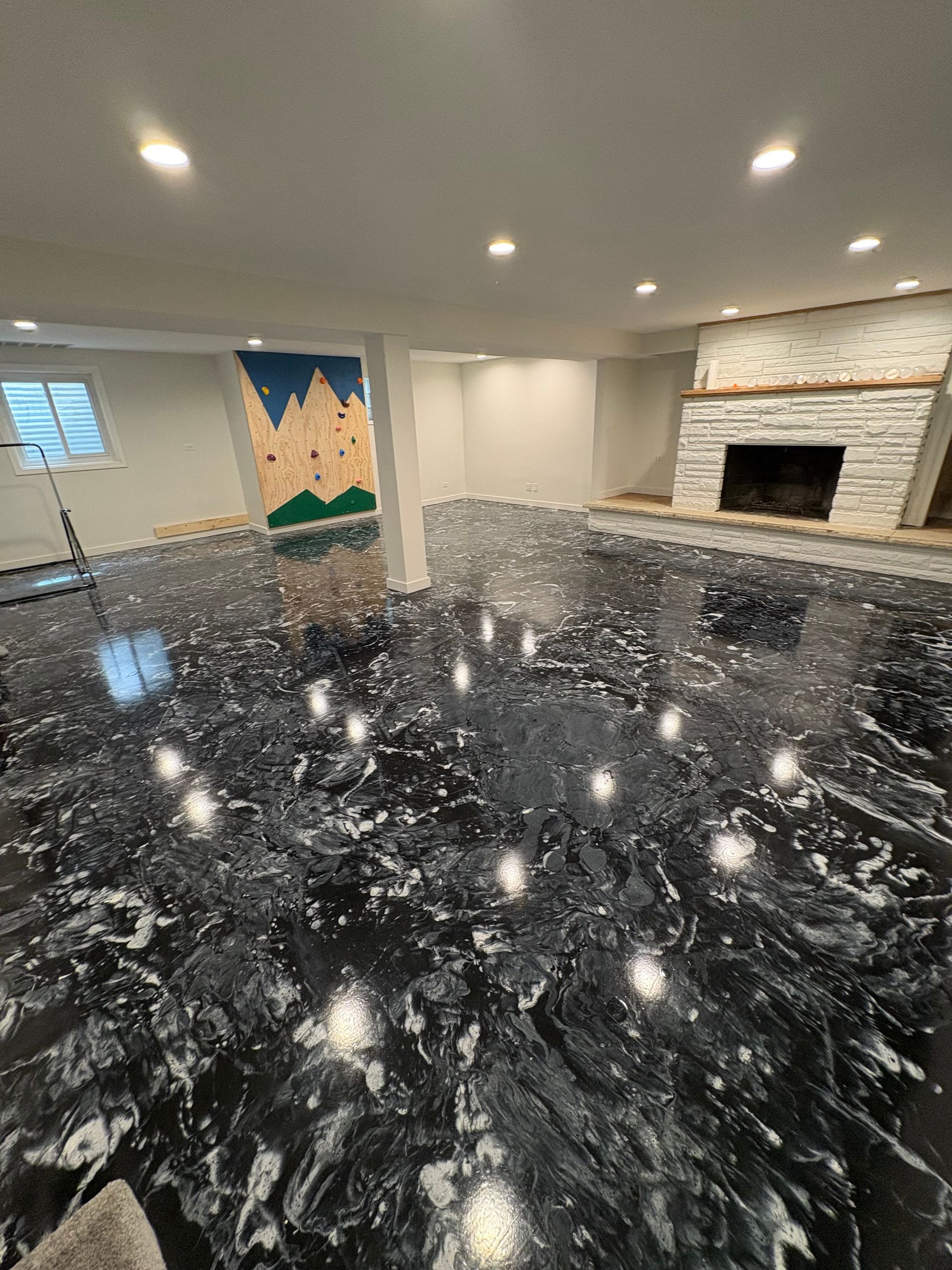 Finished basement with shiny black epoxy floor, recessed lights, and a brick fireplace.