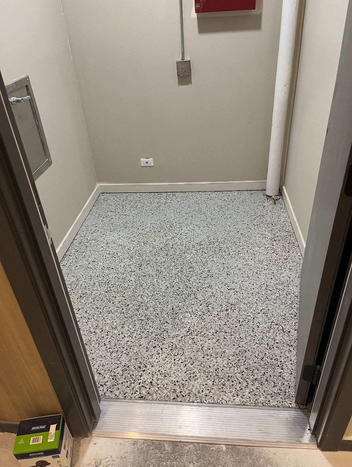A small room with a speckled gray floor, neutral walls, and a door frame.