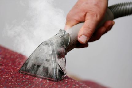 Hand using a steam cleaner on a red carpet, removing stains