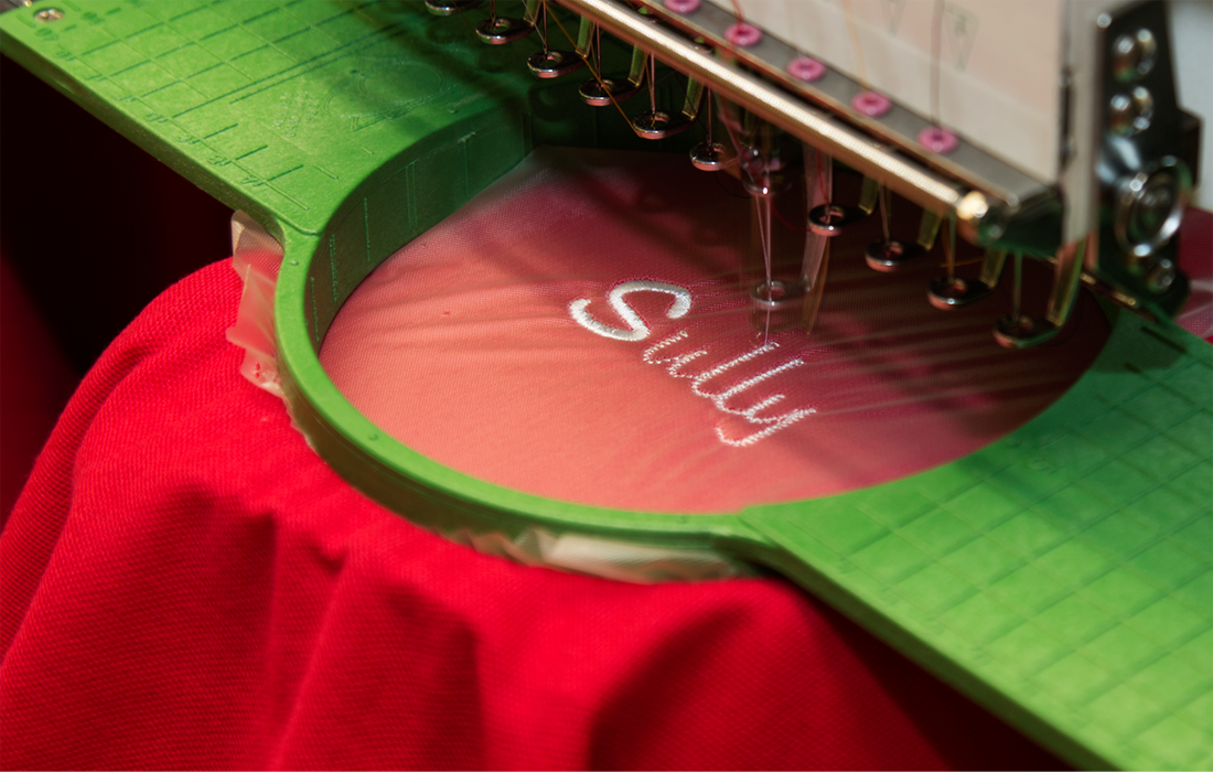 A machine is embroidery the name sally on a red shirt