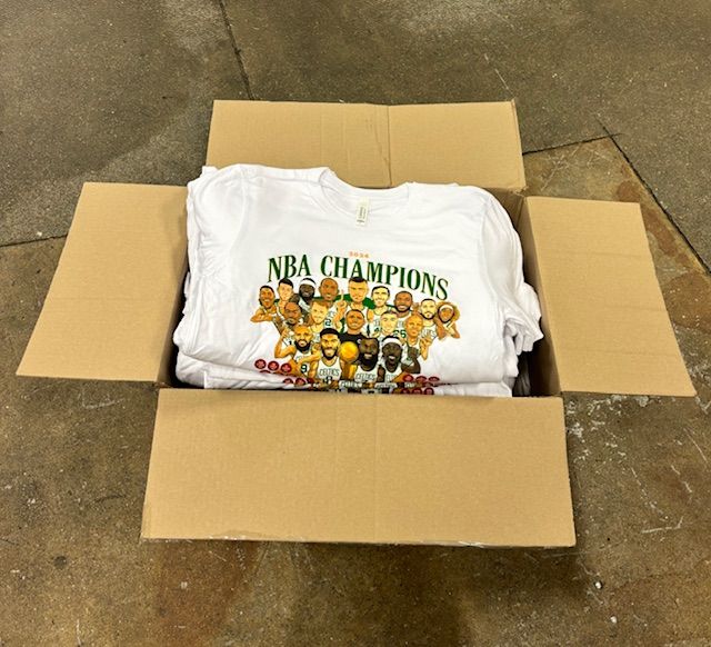 A cardboard box filled with nba champions t-shirts